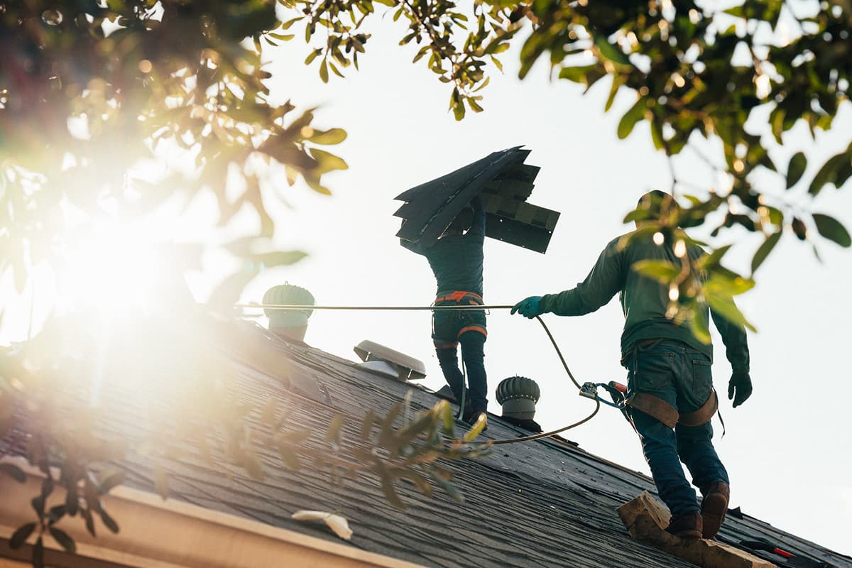 Roofers removing asphalt shingles from a home during replacement